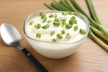 Delicious yogurt in bowl, green onions and spoon on wooden table, closeup