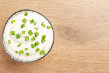 Delicious yogurt with green onions in bowl on wooden table, top view. Space for text