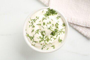 Delicious yogurt in bowl and dill on white marble table, top view