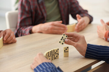 Friends playing dominoes at light wooden table, closeup
