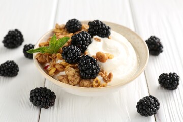 Tasty yogurt with granola and blackberries in bowl on white wooden table, closeup