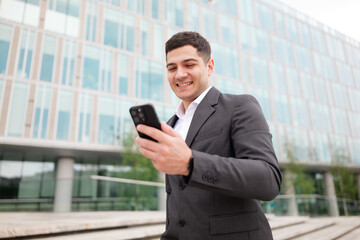 Fototapeta premium Young professional enjoying a moment of connection while checking a message on his smartphone near a modern building