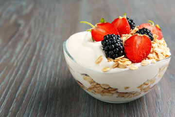 Tasty yogurt with granola and berries in bowl on wooden table, closeup. Space for text