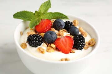 Tasty yogurt with granola and berries in bowl on white marble table, closeup