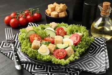 Delicious salad with croutons and ingredients on black table, closeup