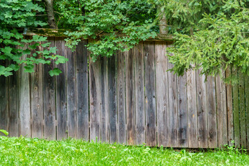 old weathered wooden fence against the background of green lawn and forest beautiful rural landscape