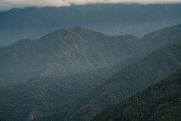 Dramatic, misty mountain range with dense green foliage.  A winding road cuts through the landscape.