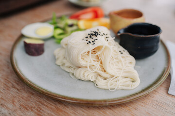 A plate of cold soba noodles with a soft-boiled egg, vegetables, and dipping sauce.