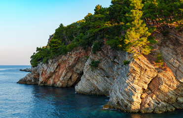 A view of cliffs along the shore of the Adriatic Sea, with forested hills in the background, located near the city of Petrovac, Montenegro.