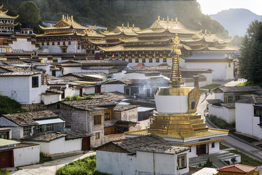 View of golden roofs gleaming atop tiered structures, nestled among simple white buildings under the soft light, creating a serene landscape, Langmu Monastery, Sichuan, China.