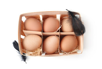 Raw chicken eggs and feathers in wooden egg tray isolated on white, top view