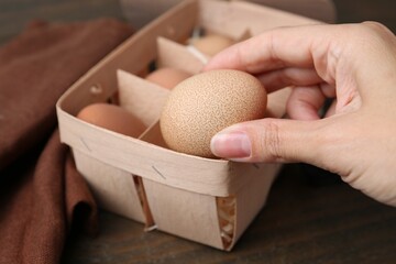 Woman taking raw chicken egg from tray at wooden table, closeup