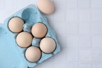 Raw chicken eggs in egg carton on white tiled table, flat lay. Space for text