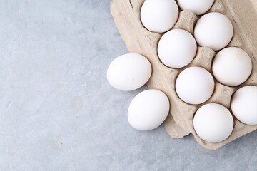 Raw chicken eggs in egg carton on grey table, top view. Space for text