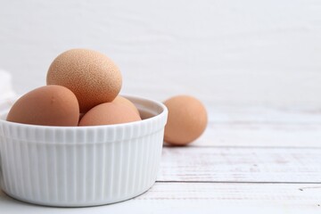 Raw chicken eggs in bowl on white wooden table, closeup. Space for text