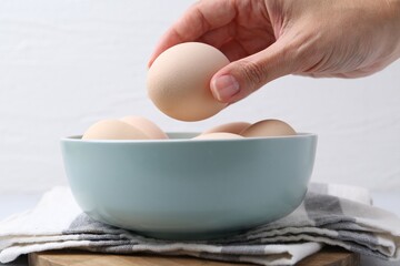 Woman taking raw chicken egg from bowl at table, closeup