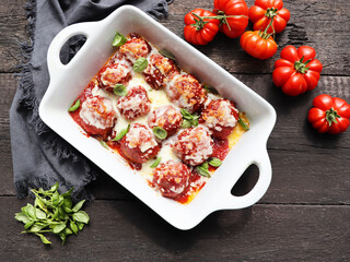 Baked cheesy meatballs casserole with tomato sauce on wooden background, top view