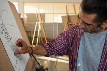 Fototapeta premium Artist is smudging charcoal sketch on drawing board on easel in art studio under window light