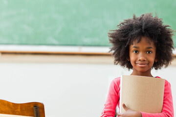 African American girl standing at school holding brown notebook by green chalkboard, copy space