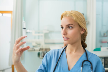 Female medical professional examining green fluid syringe in exam room with stethoscope, copy space