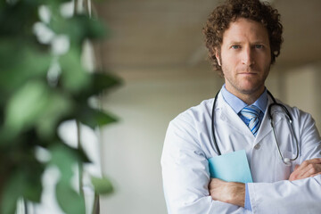 Middle-aged man in lab coat standing in hospital corridor holding stethoscope, folder, copy space