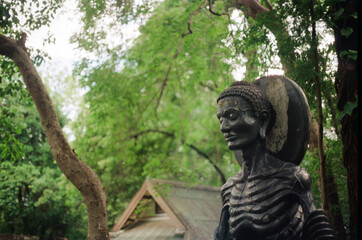 A sculpture of a fasting Buddha stands solemnly amidst lush greenery, capturing a moment of...