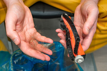 Close-up of hands holding a clump of hair and a vacuum brush roller clogged with debris. Represents...