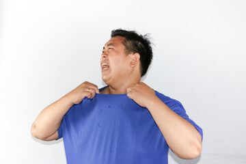 Portrait Asian man wearing blue T-shirt showing swelter gesture, hot weather, thirsty and tired over isolated white background.