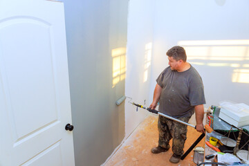 Carpenter carefully applies paint to wall with roller in home during construction area
