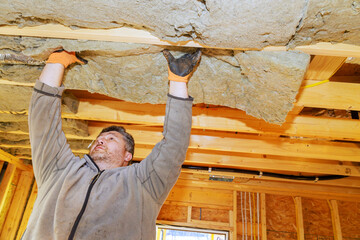 Construction worker lifts insulation material to install it in ceiling of new building under construction.