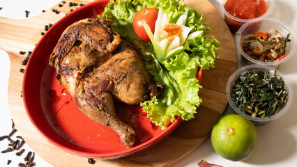 grilled chicken dish in red plate, lettuce, tomato, orange, chili sauce, cucumber and spices on the table