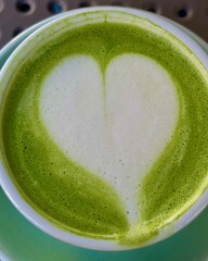 Close-up macro shot of green matcha latte tea with heart-shaped foam art and bubbles in a cup. 
