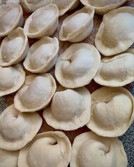 Closeup of uncooked homemade meat dumplings arranged on wooden board. 