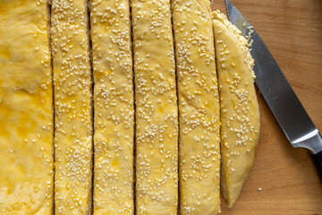 Unbaked sesame pastry strips on wooden surface
