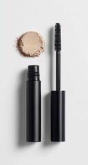 Obraz premium A beige powder spill next to a black mascara wand and its tube, set against a bright white background