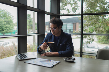 Asian businessman drinking coffee while working on his laptop at the office.