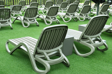 Symmetrically placed lounge chairs on synthetic green turf. Modern outdoor hotel area inviting for...
