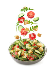 Croutons and other ingredients falling into bowl of salad against white background