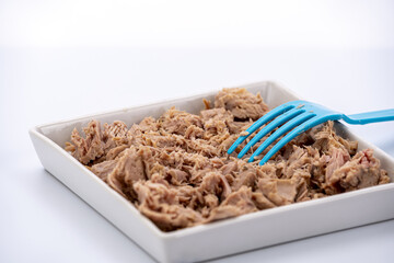 Canned tuna in brine, crushed into small pieces using a blue plastic fork.