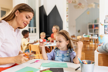 Preschool teacher engaging with children at a table during an arts and crafts activity in a bright...