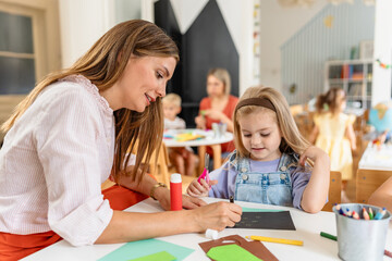 Fototapeta premium Preschool teacher guiding children from diverse backgrounds during a colorful arts and crafts activity in a bright classroom.