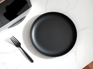 Top-down view of an empty matte black plate with a fork on a white marble. Minimalist modern table setting in natural light.