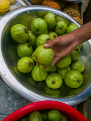 A man holds a guava, and the background is blurred