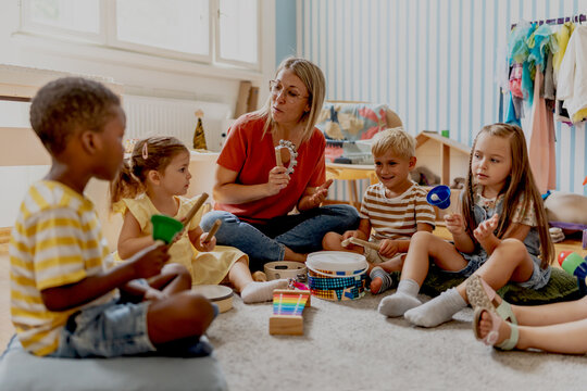 Preschool teacher leading a fun interactive activity with children sitting in a circle, raising hands and smiling in a bright classroom
