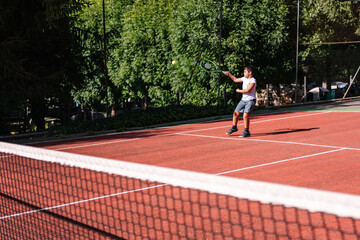 Concentrated boy executing a powerful serve during an exciting tennis match on a bright, sunny day...