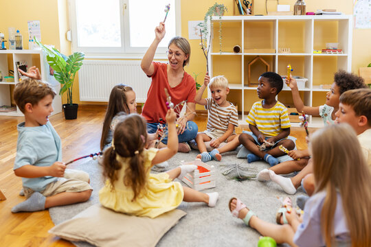 Preschool teacher leading a fun interactive activity with children sitting in a circle, raising hands and smiling in a bright classroom