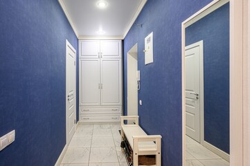 blue-walled hallway with white accents, including a built-in wardrobe, a bench, and a mirror...
