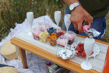 Elegant picnic setup with gourmet snacks, desserts, and sparkling wine served outdoors on a wooden table, perfect summer celebration concept.