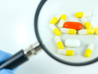 A magnifying glass over a variety of pills on a white background
