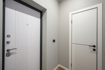 modern entryway with two white doors, one ornate with a peephole and steel hardware, the other...